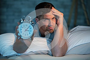 insomniac man in bed showing alarm clock