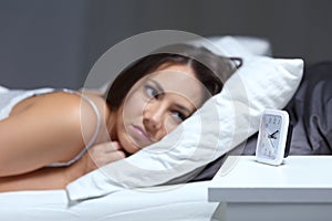 Insomniac woman looking at alarm clock in the night photo