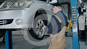 Inspection of the chassis of the car. A young mechanic in uniform works in a car service with a lifted car. Car repair