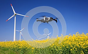 Inspection drone with eolian turbines behind. Rapeseed field in bloom. Renewable energy