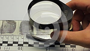 Inspection of a fingerprint card under a magnifying glass close-up.