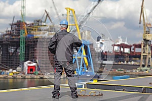 Inspector in coveralls and hardhat standing on harbor wharf.