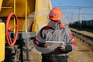 Inspector of wagons at freight train station makes notes in tablet computer