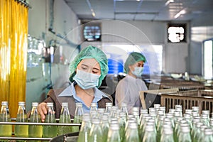 Inspector woman checking a bottled fruit beverage on conveyer production line in processing beverage factory