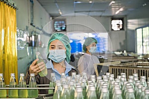 Inspector woman checking a bottled fruit beverage on conveyer production line in processing beverage factory