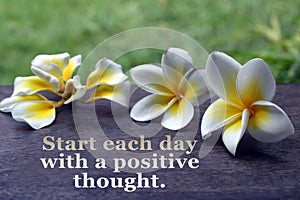 Inspiratieonal quote - Start each day with a positive thought. On Bali plumeria flower on green and wooden board backgrounds.