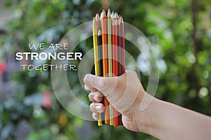 Inspiratinal motivational quote - We are stronger together. With young woman hand holds bunch of pencil colored and blurry green.