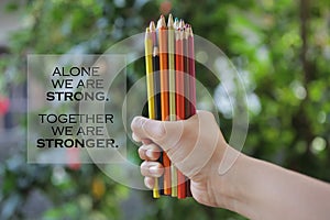 Inspiratinal quote - Alone we are strong. Together we are stronger. With young woman hand holds bunch of pencil colored and blurry