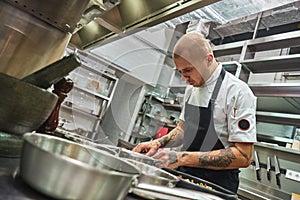 Inspiration in cooking. Young male chef with several tattoos on his arms is garnishing italian pasta in a restaurant
