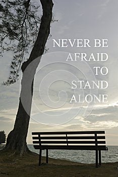 Inspiration motivational quotes with single bench and a tree on a hill during sunset. Never be afraid to stand alone