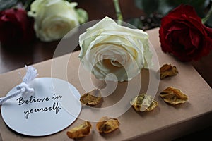 Inspirational motivational - Believe in yourself. On background of tag label paper with text message, white and red roses.