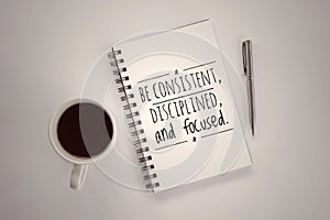 Inspirational motivational quote - Be consistent, disciplined and focused. Text message on a spiral notebook with pen, coffee cup.