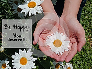 Inspirational motivational quote - Be happy. You deserve it. With beautiful white daisy flower blossom in young woman hand.