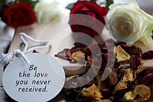 Inspirational motivational quote - Be the love you never received. With text message written on tag label paper with roses.