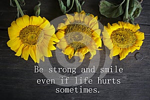 Inspirational motivational quote - Be strong and smile even if life hurts sometimes. With yellow sun flowers decoration on rustic photo