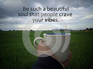 Inspirational motivational quote - Be such a beautiful soul that people crave your vibes. With person holding coffee cup in field. photo