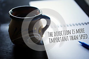 Inspirational motivational quote - The direction is more important than speed. Text message on paper book with a cup of coffee.