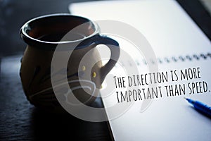 Inspirational motivational quote - The direction is more important than speed. Text message on paper book with a cup of coffee. photo