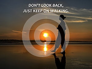 Inspirational motivational quote - Don`t look back, just keep on walking. With silhouette of a woman walking alone on the beach.