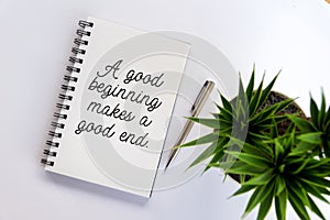 Inspirational motivational quote - A good beginning makes a good end. With book, pen and plant on white table background.