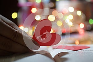Inspirational motivational quote - Spread love. With red heart in hand. Valentine day card concept on colorful bokeh lights