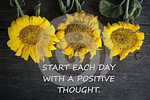 Inspirational motivational quote - Start each day with a positive thought. With yellow sun flowers on rustic wooden table