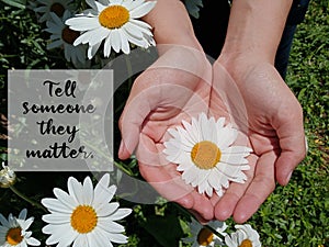 Inspirational motivational quote - Tell someone they matter. With background of big white daisy flower blossom in young woman hand