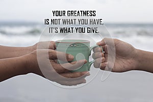 Inspirational motivational quote - Your greatness is not what you have. It is what you give. With hands holding coffee cup. photo