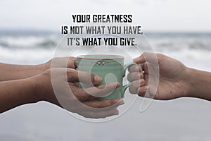 Inspirational motivational quote - Your greatness is not what you have. It is what you give. With hands holding coffee cup.