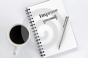 Inspirational motivational words - Improve yourself, on a spiral notepaper book with silver pen and a cup of black morning coffee. photo