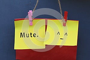 Inspirational note quote - Mute. With mute face emoticon on colorful origami paper hanging on wall with pin and rope.