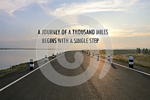 Inspirational positive quote `A journey of a thousand miles begins with a single step` on a road and water reservior background.