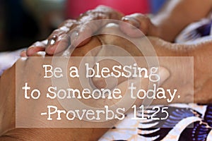 Inspirational quote - Be a blessing to someone today. Proverbs 11.25. On background of women holding hands on lap.