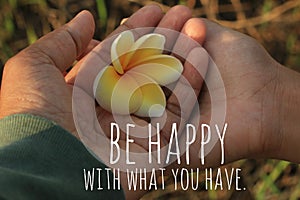 Inspirational quote - Be happy with what you have.  On background of two hands of mom and daughter holding Bali frangipani flower.