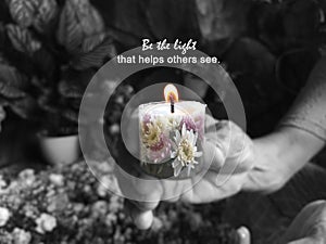 Inspirational quote - Be the light that helps others see. Senior woman holding candle light in hand with spring flowers pattern.