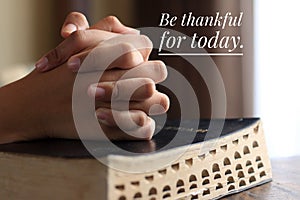 Inspirational quote - Be thankful for today. With background of young woman clenched prayer hands on a bible book.