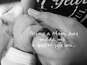 Inspirational quote- Being a Mom has made me a better person. With blurry image of a fragile little baby new born hand and fingers