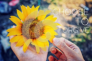 Inspirational quote - Choose to forgive. With sunflower in the hand. Forgiveness concept with young girl holding a yellow flower.