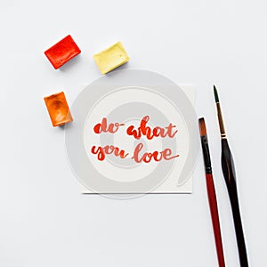 Inspirational quote do what you love , watercolor cuvettes, paint brushes on a white background. Artist workspace.