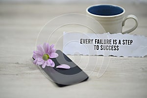 Inspirational quote - Every failure is a step to success. With morning cup of coffee and purple daisy flower on black phone.