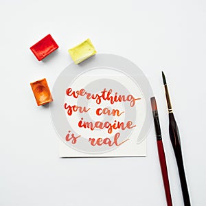 Inspirational quote everything you can imagine is real , watercolor cuvettes, paint brushes on a white background.