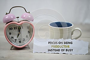 Inspirational quote - Focus on being productive instead of busy. With alarm table clock and a cup of morning coffee.