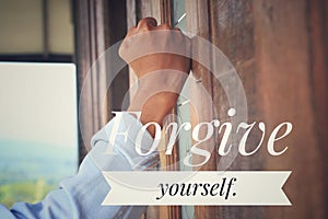 Inspirational quote - Forgive yourself. With an emotional gesture of a man hand clenched fist on the wooden window or wall.