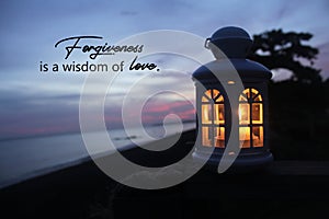 Inspirational quote - Forgiveness is a wisdom of love. With white lantern and the candle light inside on wood in the beach.