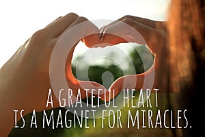 Inspirational quote  - A grateful heart is a magnet for miracles. With young woman hands making love sign against the sunset light photo