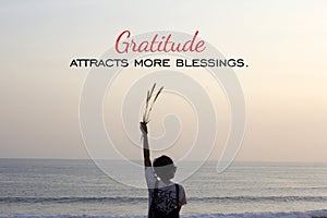 Inspirational quote - Gratitude attracts more blessings. With young woman standing alone in the beach, watching sunset over ocean.