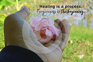 Inspirational quote - Healing is a process. Forgiveness is the beginning. With woman holding pink flower in hand closeup.