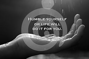 Inspirational quote - Humble yourself or life will do it for you. On abstract background of hand receiving light in black white.