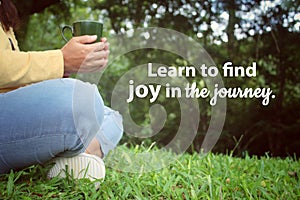Inspirational quote - Learn to find joy in the journey. With relax legs of a woman sitting alone in the park with glass in hands.