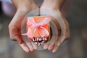 Inspirational quote - Life is a gift. With small orange gift box in hand. Gratitude, thankfulness concept with a gift.